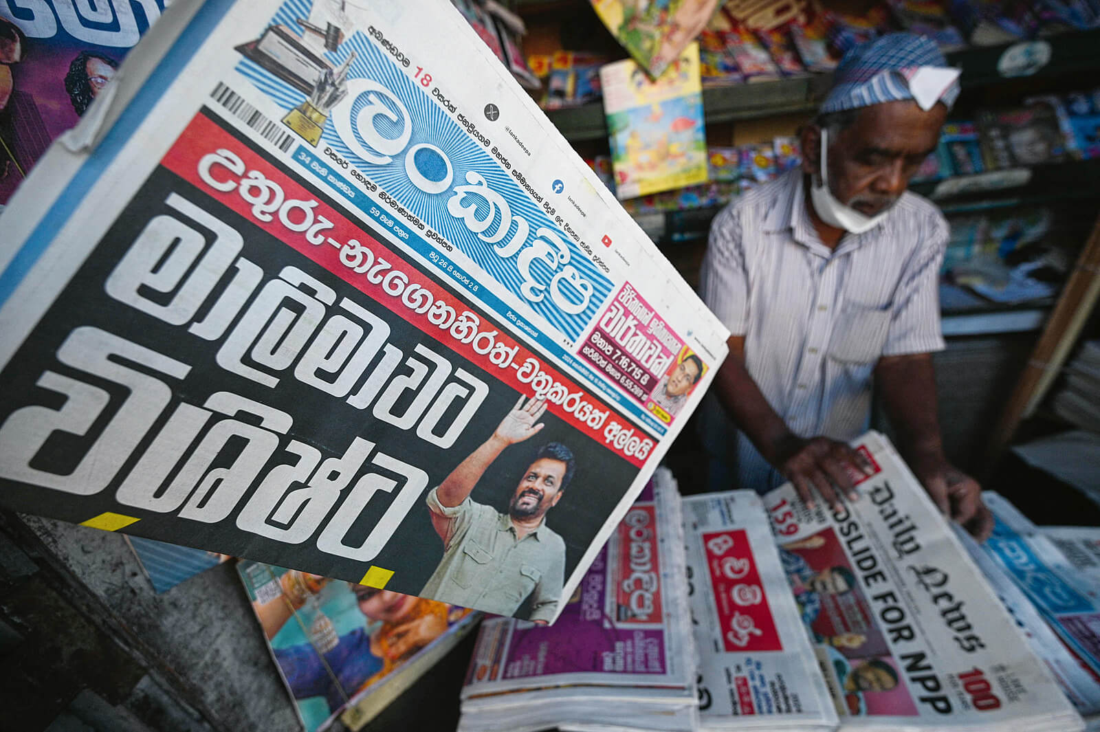 Foto einer Zeitung aus Sri Lanka, die von einem älteren Mann an einem Zeitungsstand verkauft wird.
