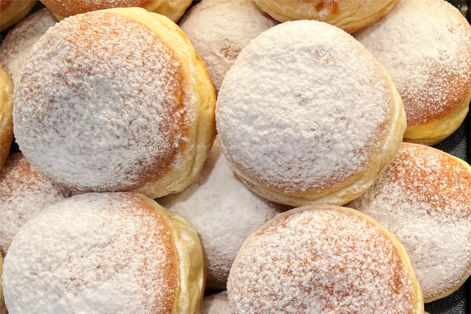 Zahlreiche mit Puderzucker bestreute Krapfen übereinander.