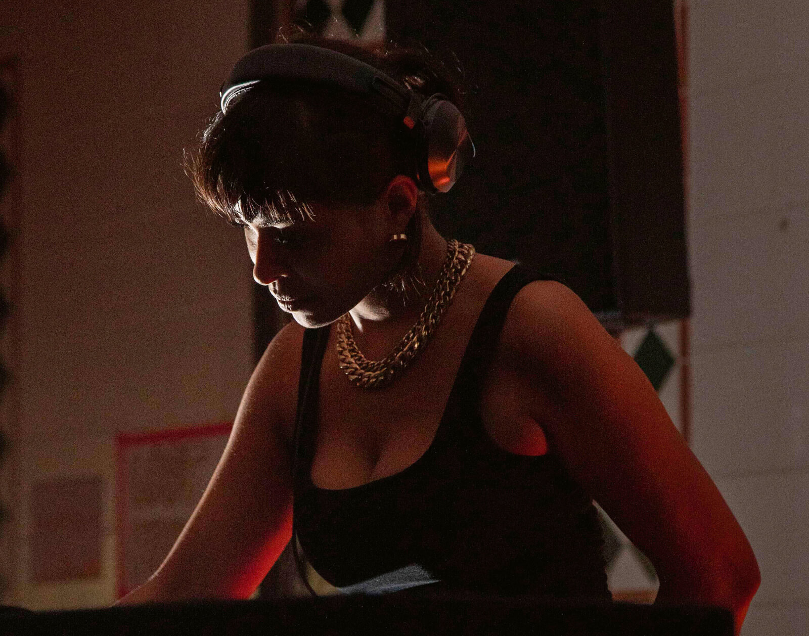 Porträt der Musikerin Lucy Bakanal: Eine Frau mit Kopfhörern steht konzentriert am DJ-Pult.