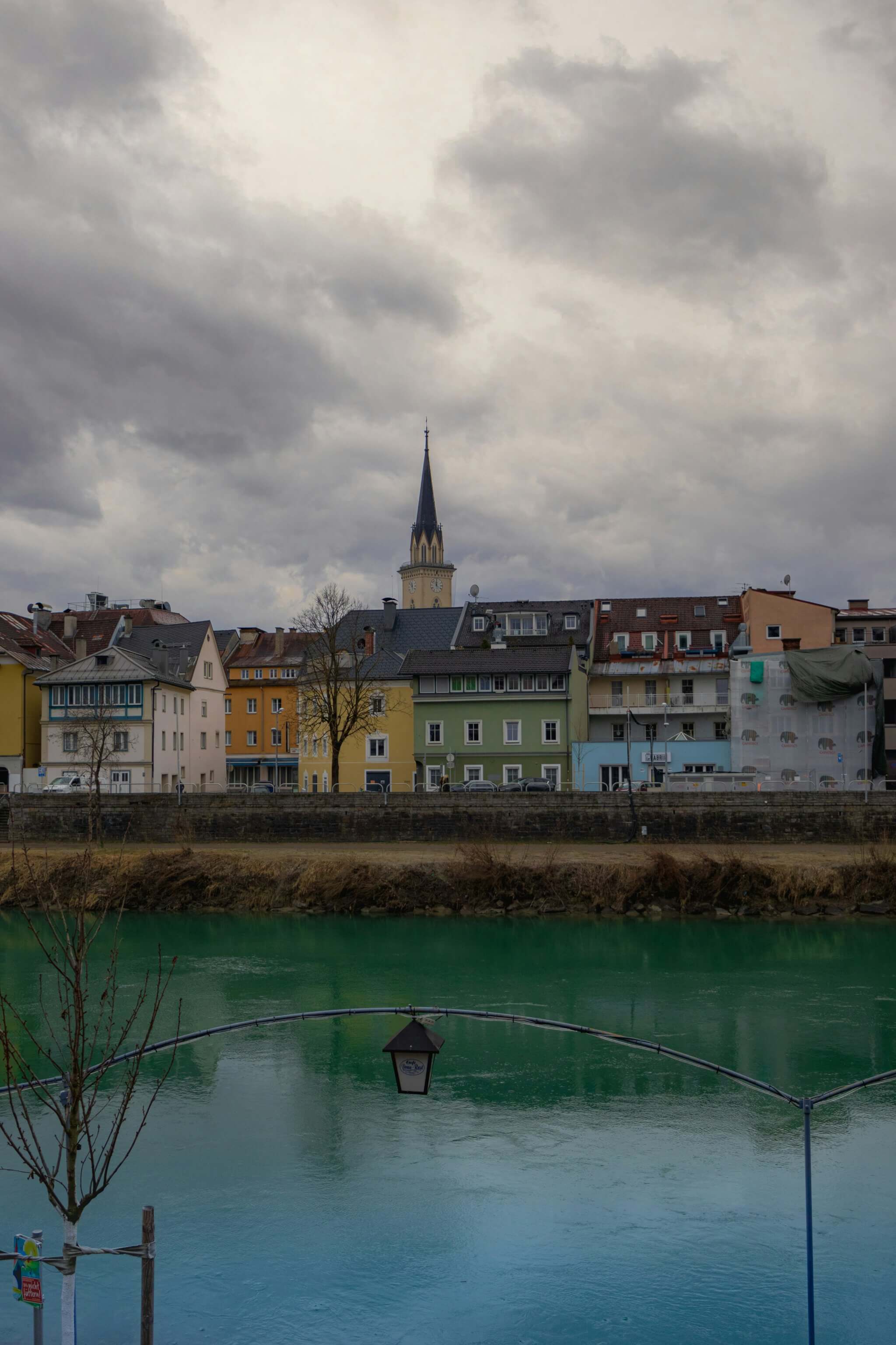 Bunte Häuser mit einem Kirchturm im Hintergrund, davor ein Gewässer.