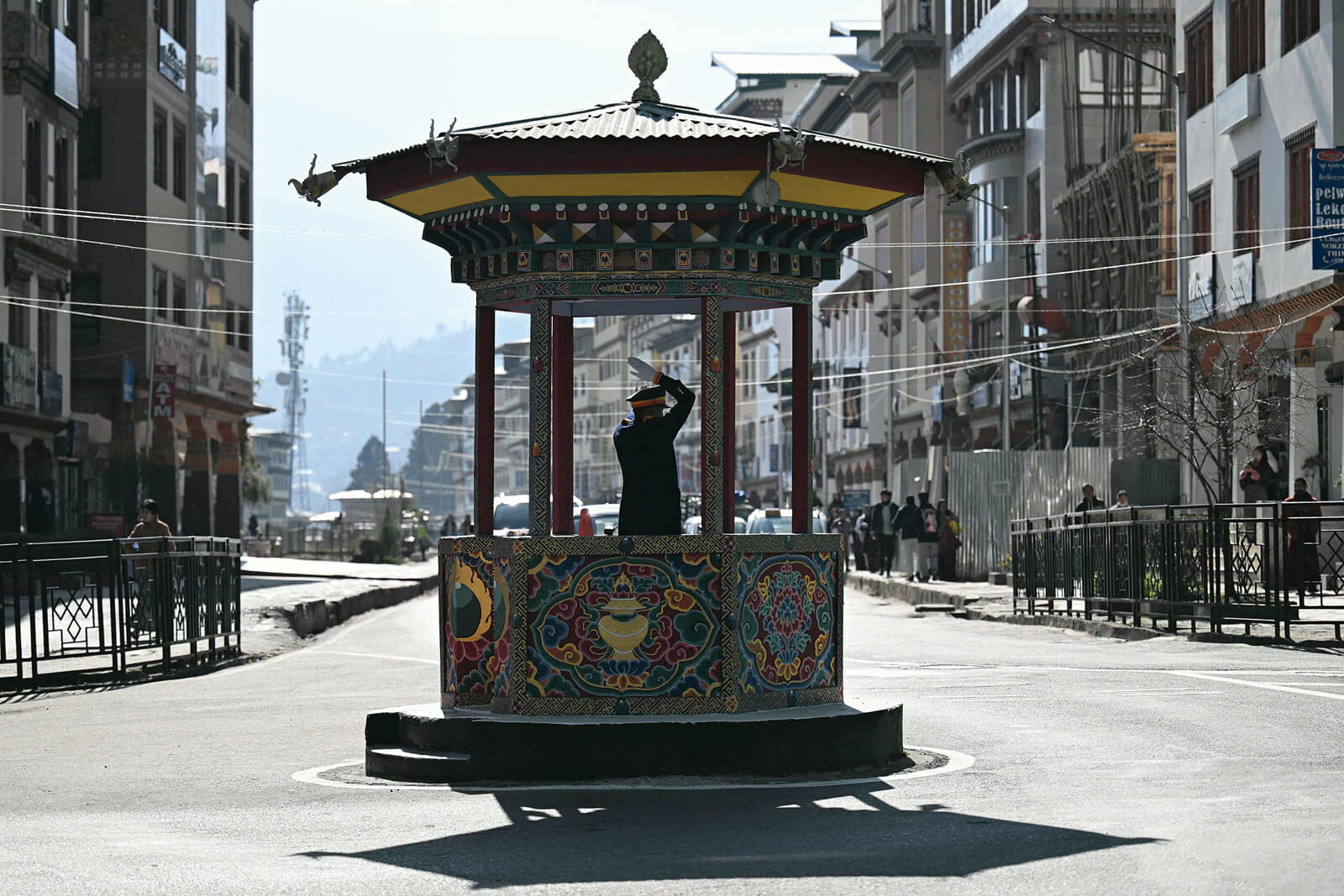 Person steht in einem farbenfroh verzierten Pavillon in der Mitte einer leeren Straße zwischen Gebäuden.