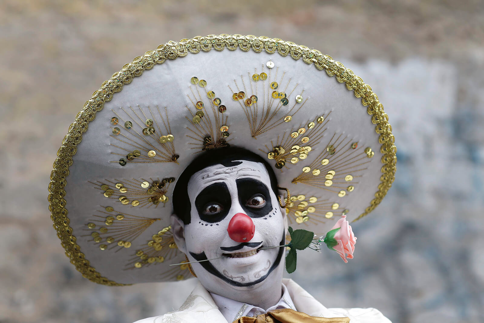 Ein als Clown verkleideter Mann mit großem Hut und einer Rose im Mund.