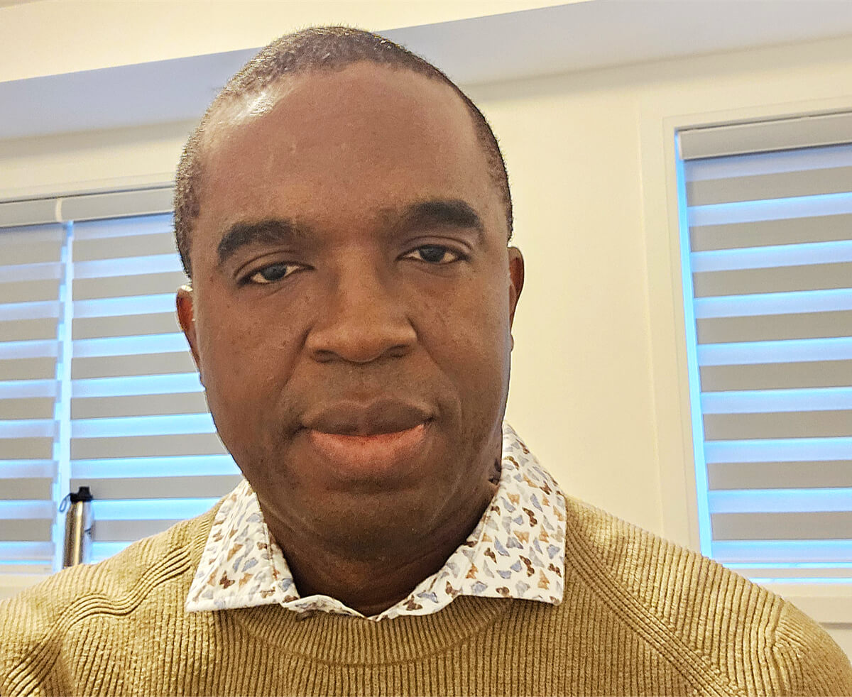 Porträt des Anthropologen Izuu Nwankwo: Ein Mann mit Hemd und hellbraunem Pullover.