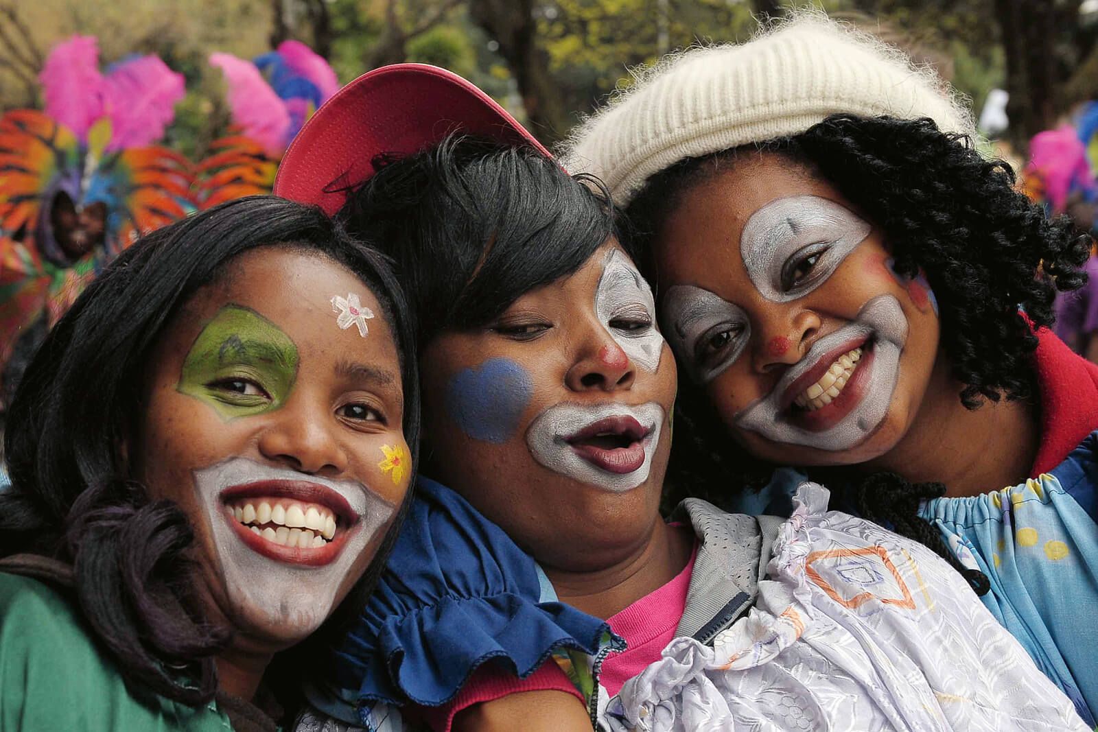 Drei Frauen mit aufgemalten Clownsgesichtern stecken die Köpfe zusammen.