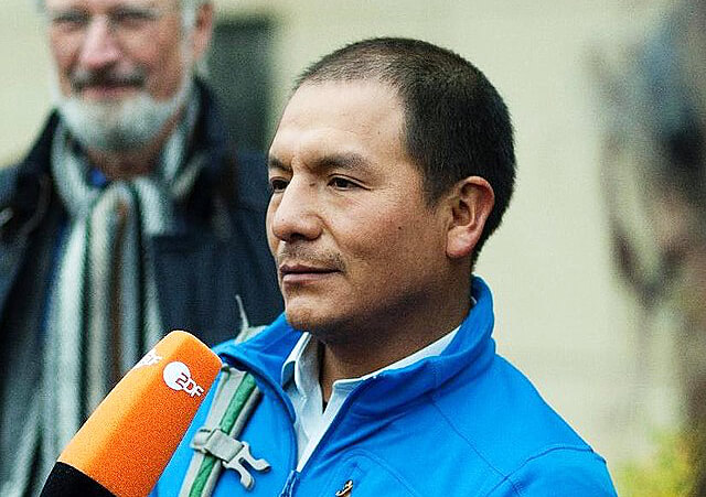 Porträt von Saúl Luciano Lliuya: Einem Mann mit blauer Jacke und kurzen Haaren wird ein orangenes Mikrofon für ein Interview hingehalten.