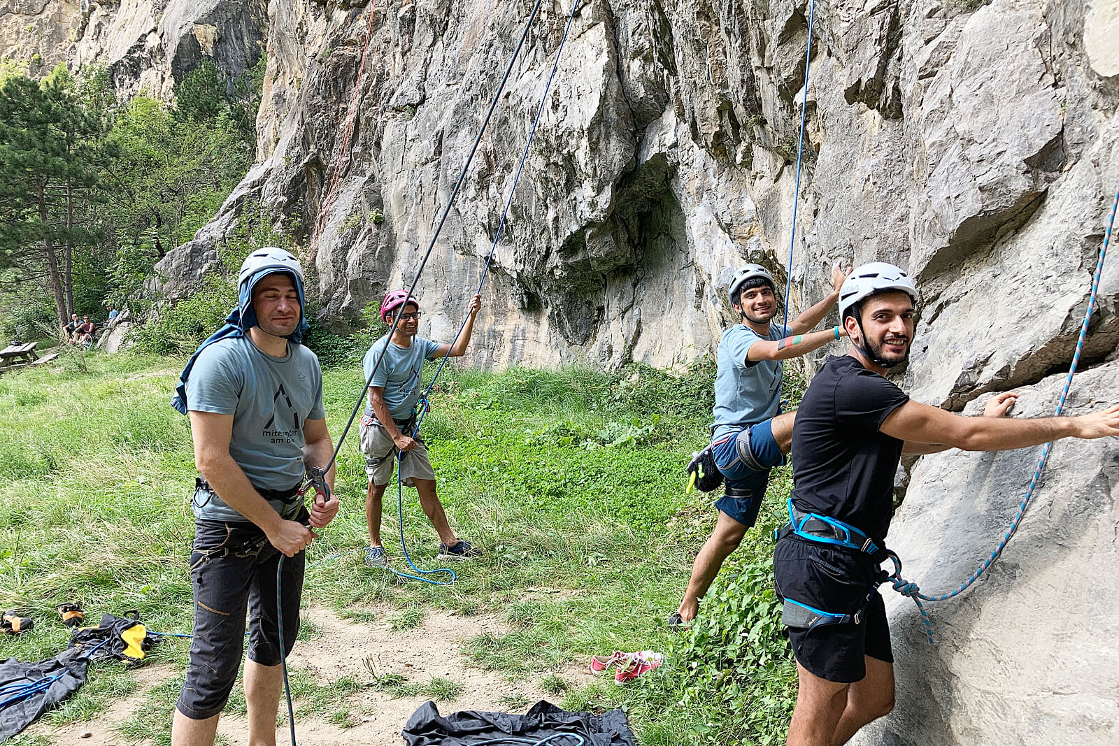 Vier Kletterer am Beginn eines Kletteraufstiegs an einer steilen, grauen Felswand.