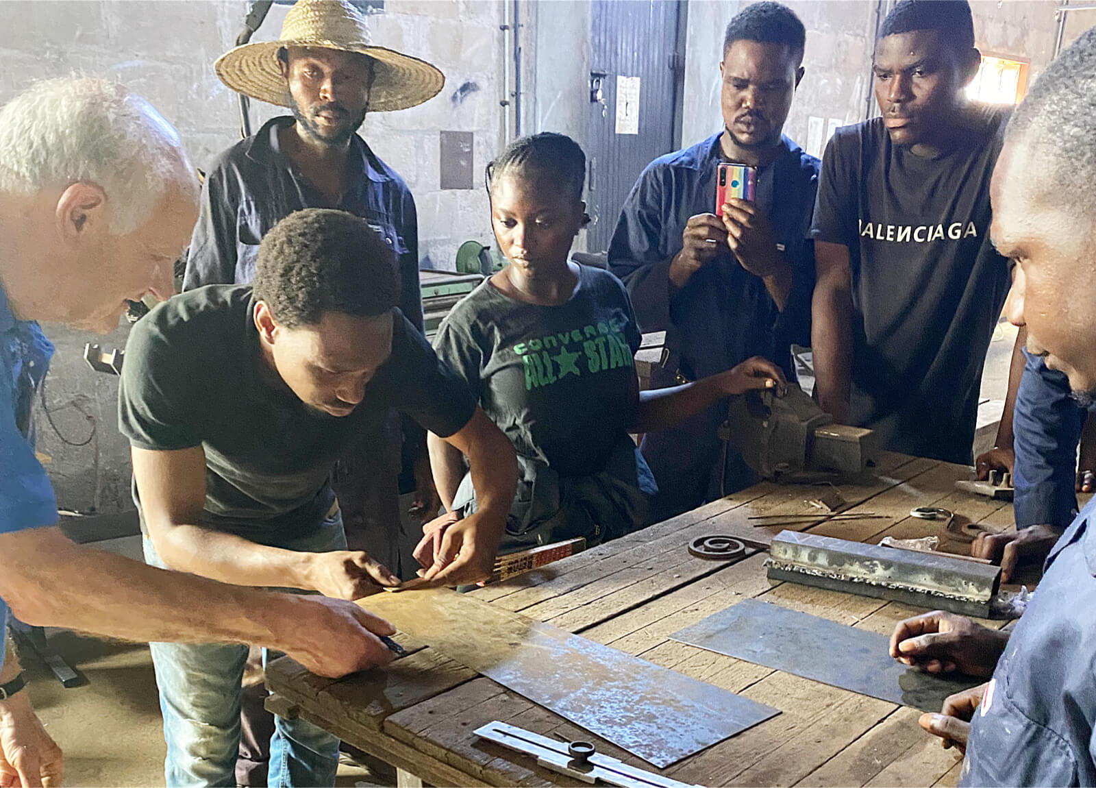 Gruppe von Menschen in Werkstatt, die an Metallarbeiten auf einem Holztisch zusammenarbeiten.
