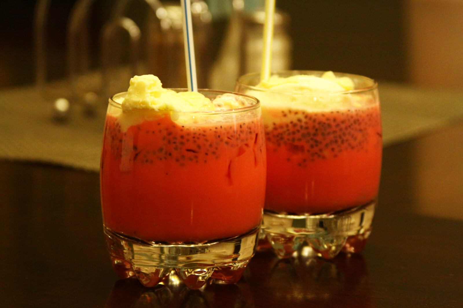 Zwei Gläser mit rotem Falooda-Getränk, garniert mit Sahne und Basilikumsamen, mit Strohhalmen.