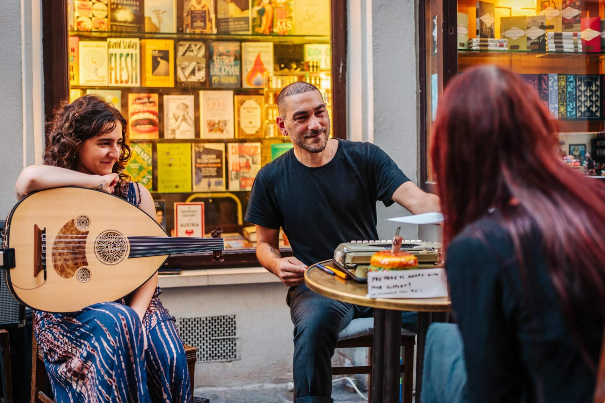Ox Maló beim Porträtieren einer Person, eine Musikerin mit Gitarre sitzt daneben