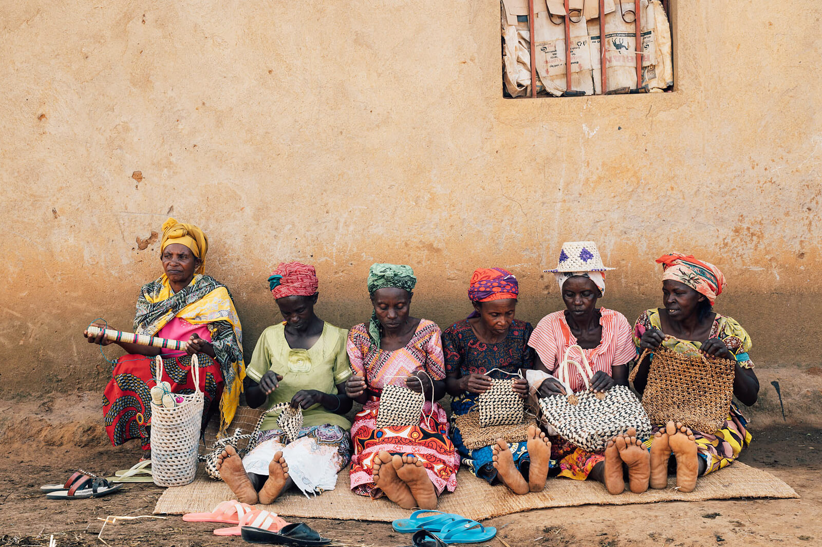Mehrere Frauen sitzen an einer Wand und flechten bunte Körbe.