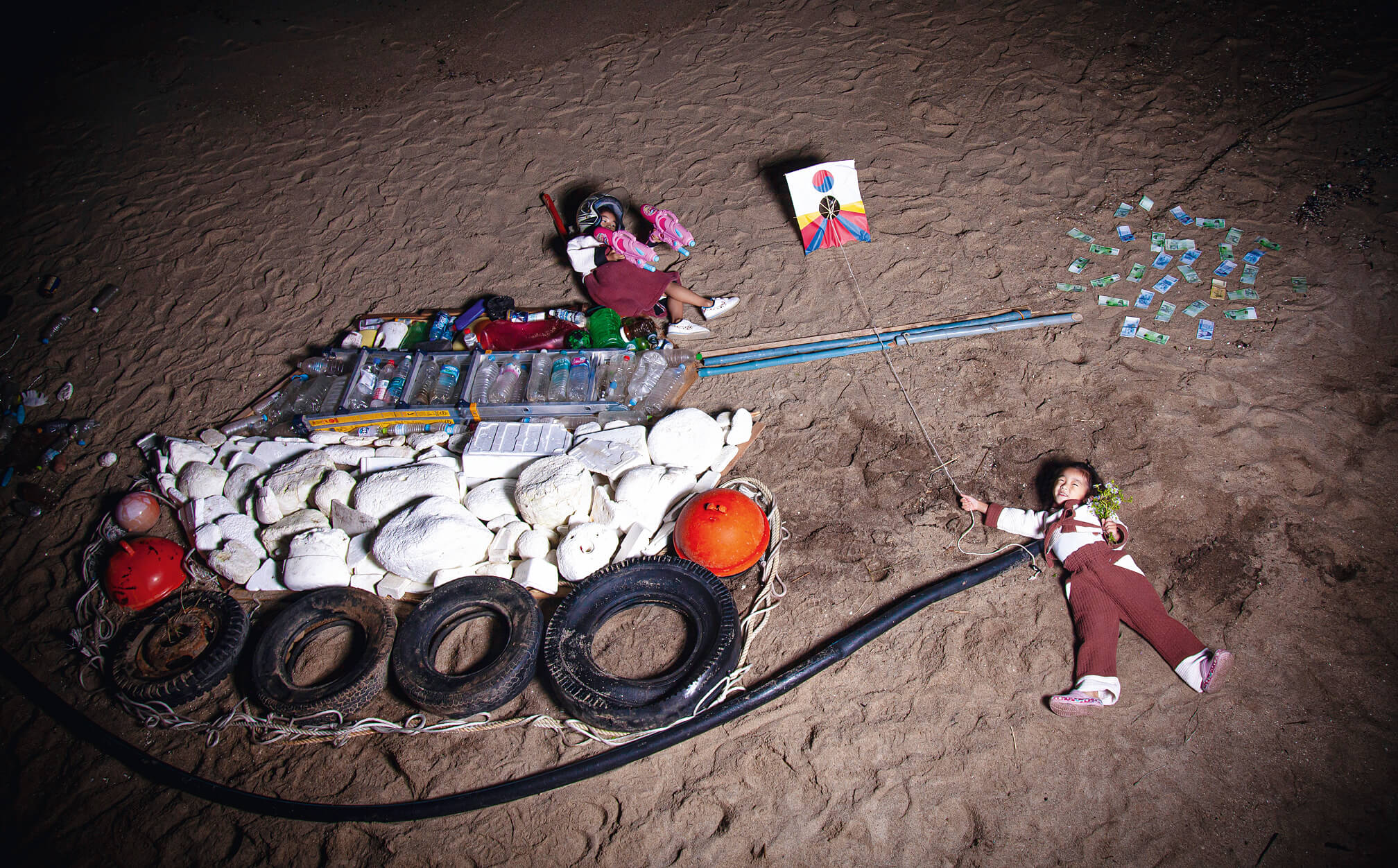 Kinder liegen im Sand neben einem Panzer aus Müll und halten einen Drachen.