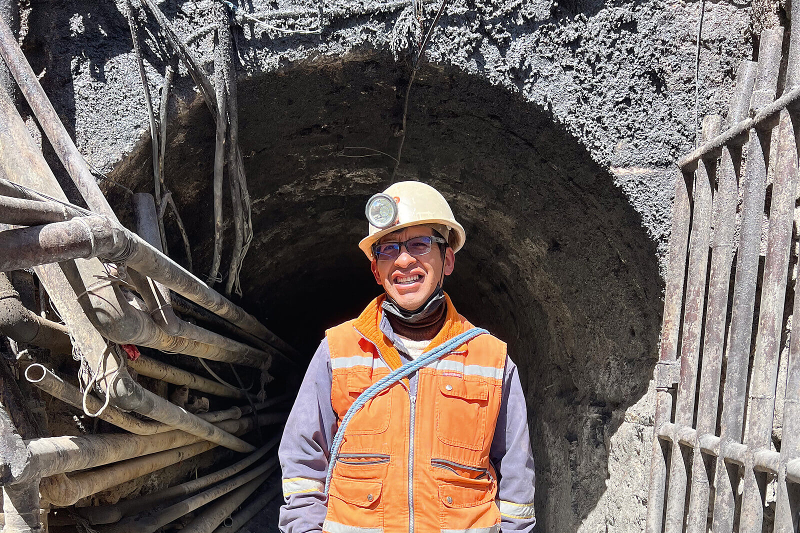 Mann mit Schutzhelm und Warnweste steht vor dem Eingang eines Bergwerks.
