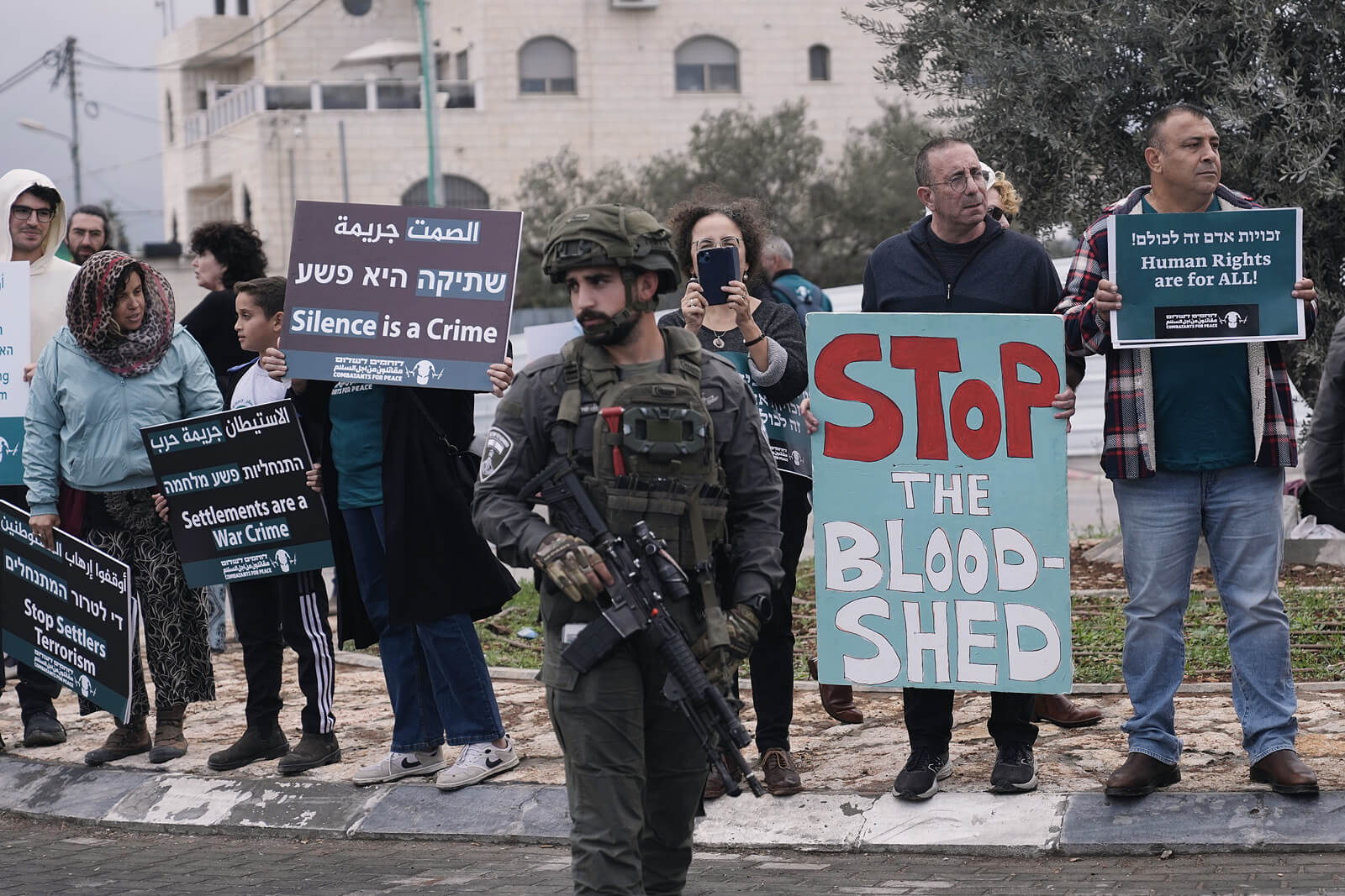 Demonstrierende Menschen mit Protestschildern, im Vordergrund ein bewaffneter Soldat.