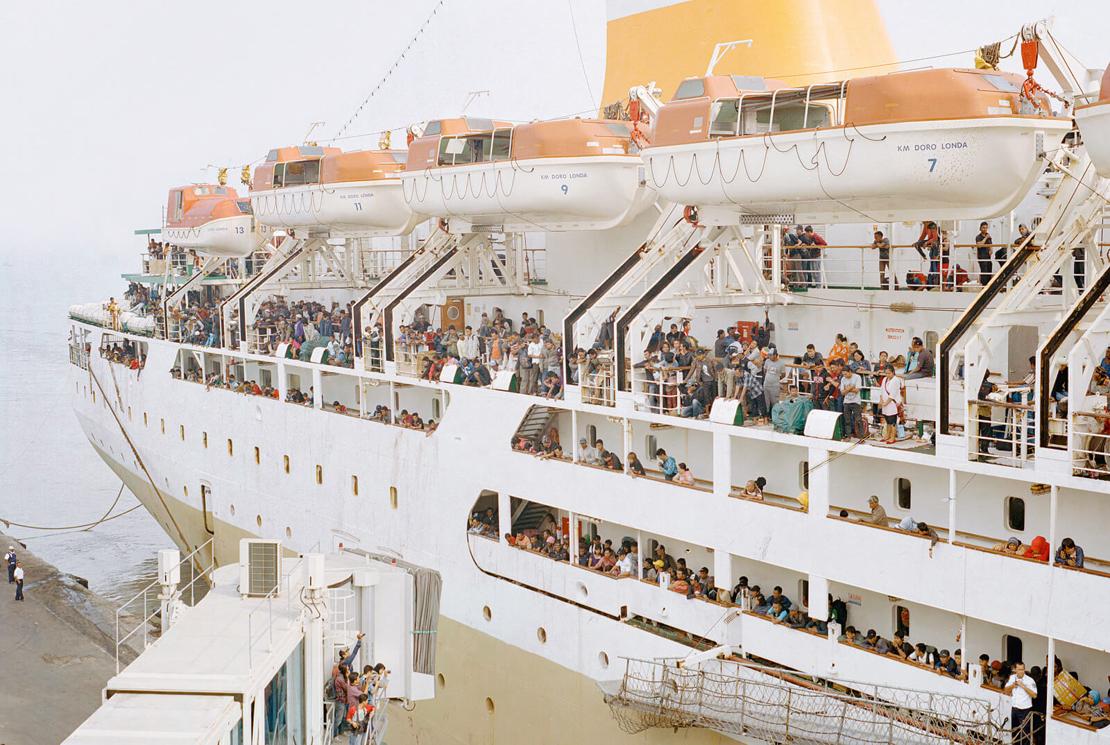 Großes Passagierschiff mit vielen Menschen an Deck und Rettungsbooten entlang der Seite.