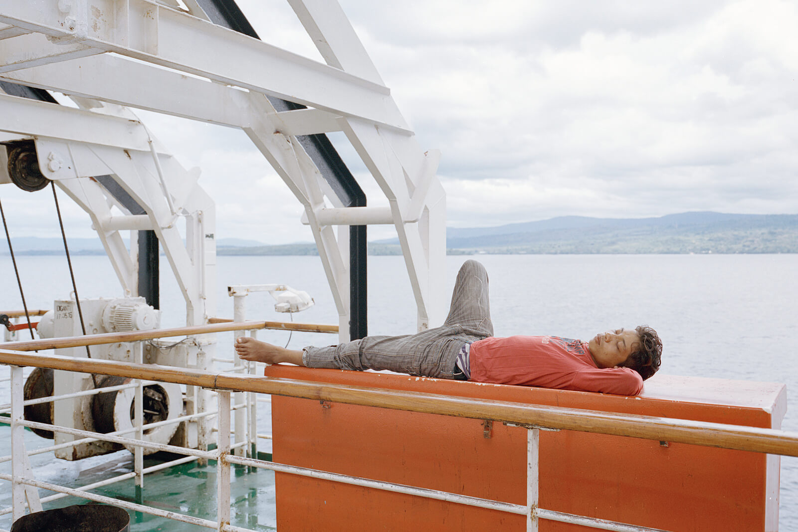 Person liegt entspannt auf einer Bank an Deck eines Fährschiffs mit Blick auf das Meer.