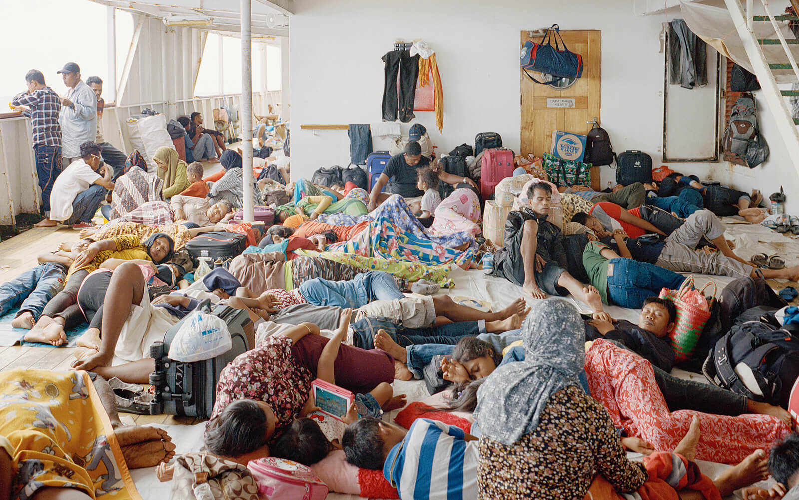 Viele Menschen liegen dicht gedrängt mit Gepäck auf dem Boden im Inneren eines Fährschiffs.
