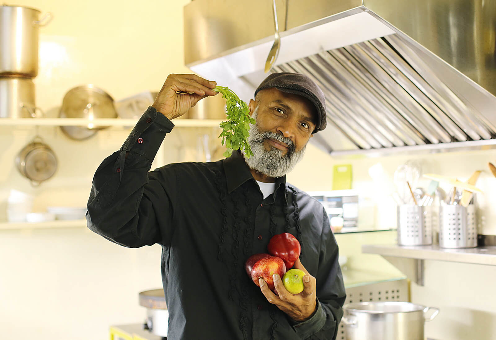 Porträt von Allan Kräuter in einer Küche, der Kräuter und Obst in den Händen hält.