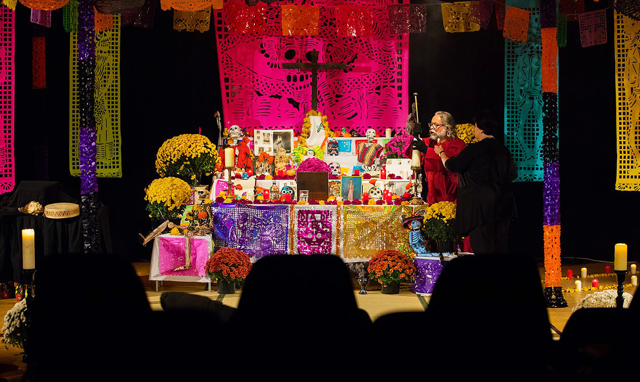 Kunstvoll geschmückter Altar zum Día de los Muertos mit Kerzen, Blumen, Totenköpfen und bunten Papiergirlanden.